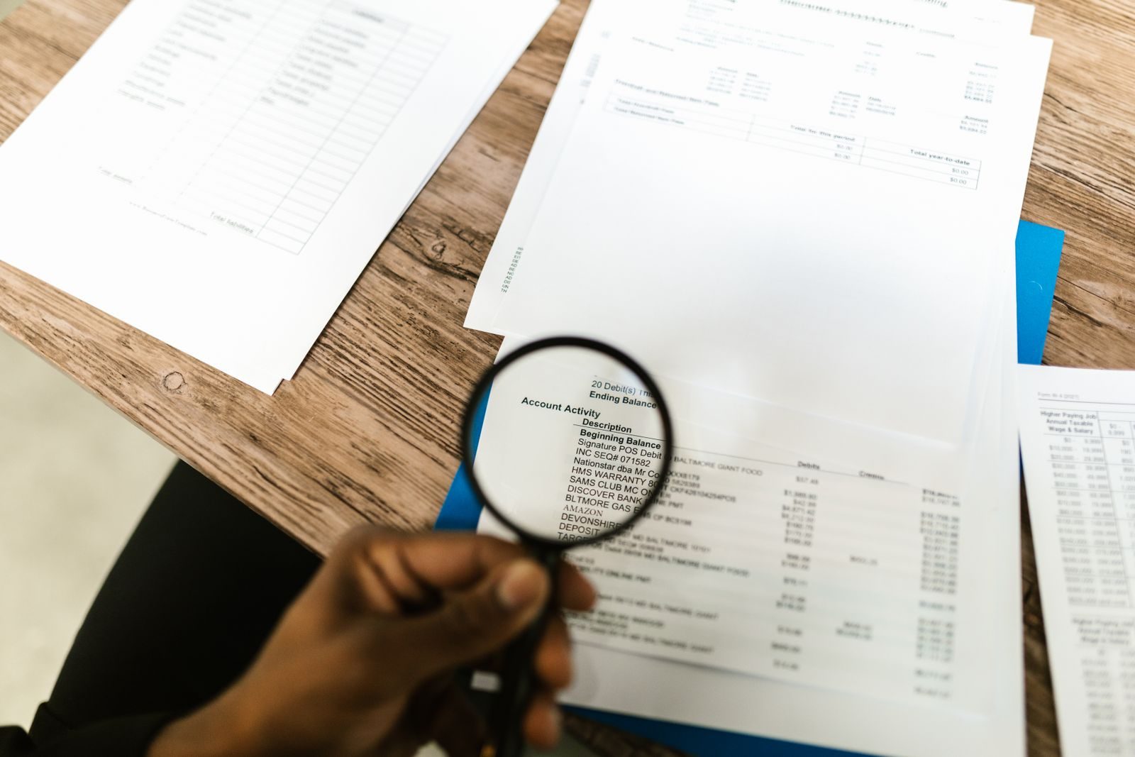 Une main tient une loupe au-dessus de documents posés sur une table