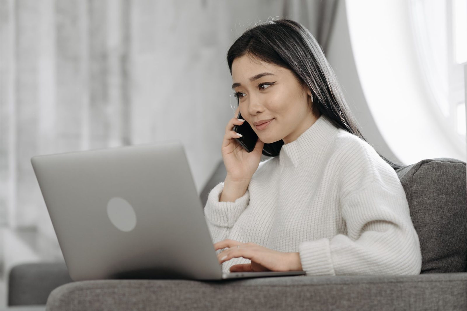 Femme au téléphone chez elle, un ordinateur portable sur les genoux