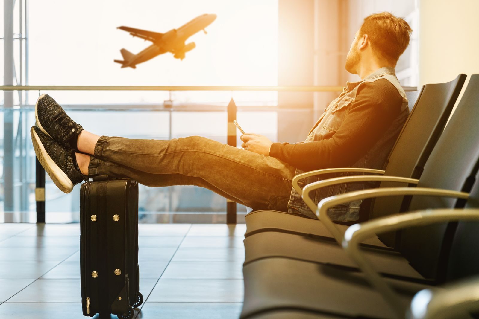 Un voyageur attend dans un terminal d'aéroport, un avion décolle derrière la vitre