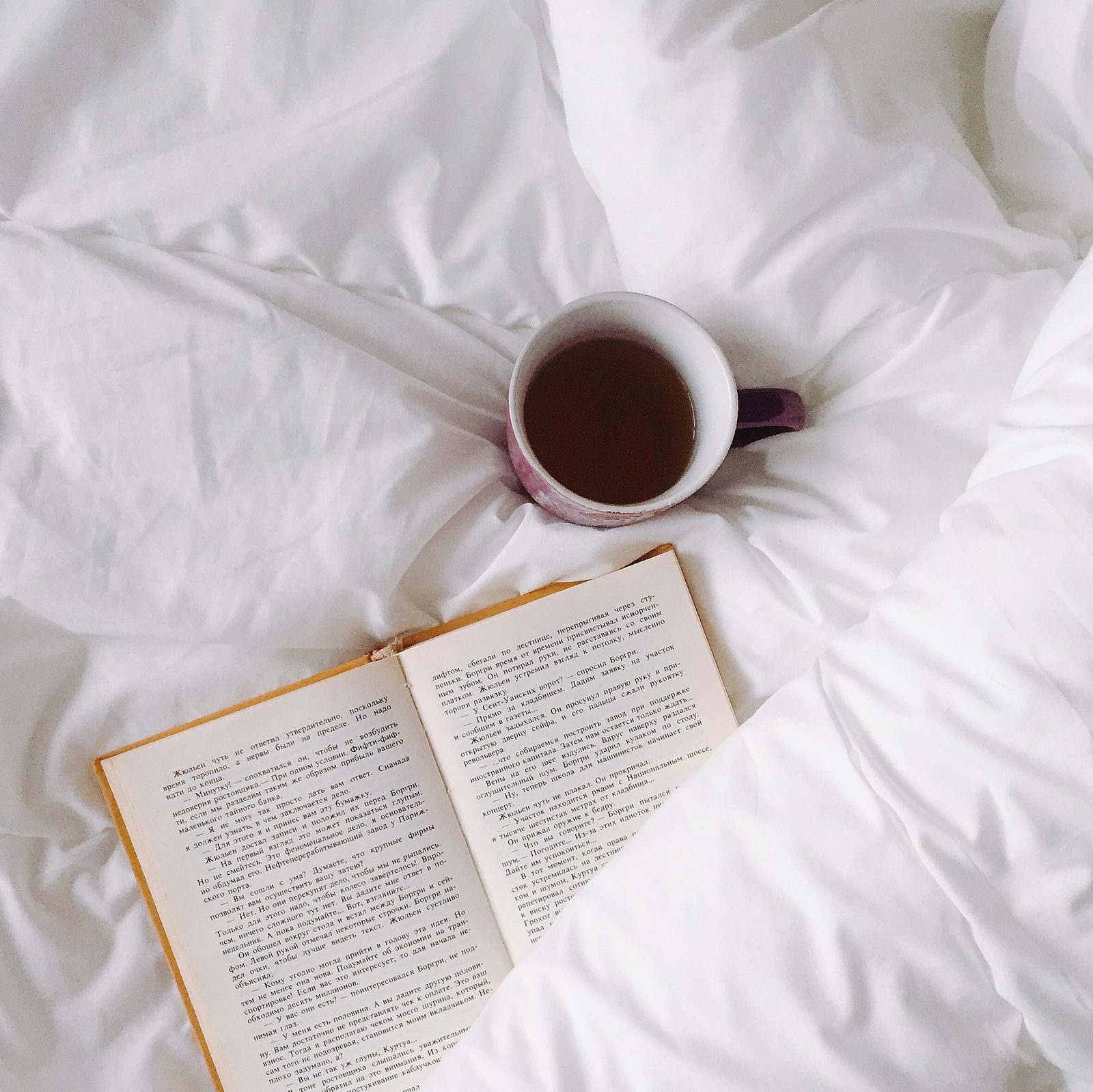 Une tasse de thé et un livre ouvert posés sur une couette blanche
